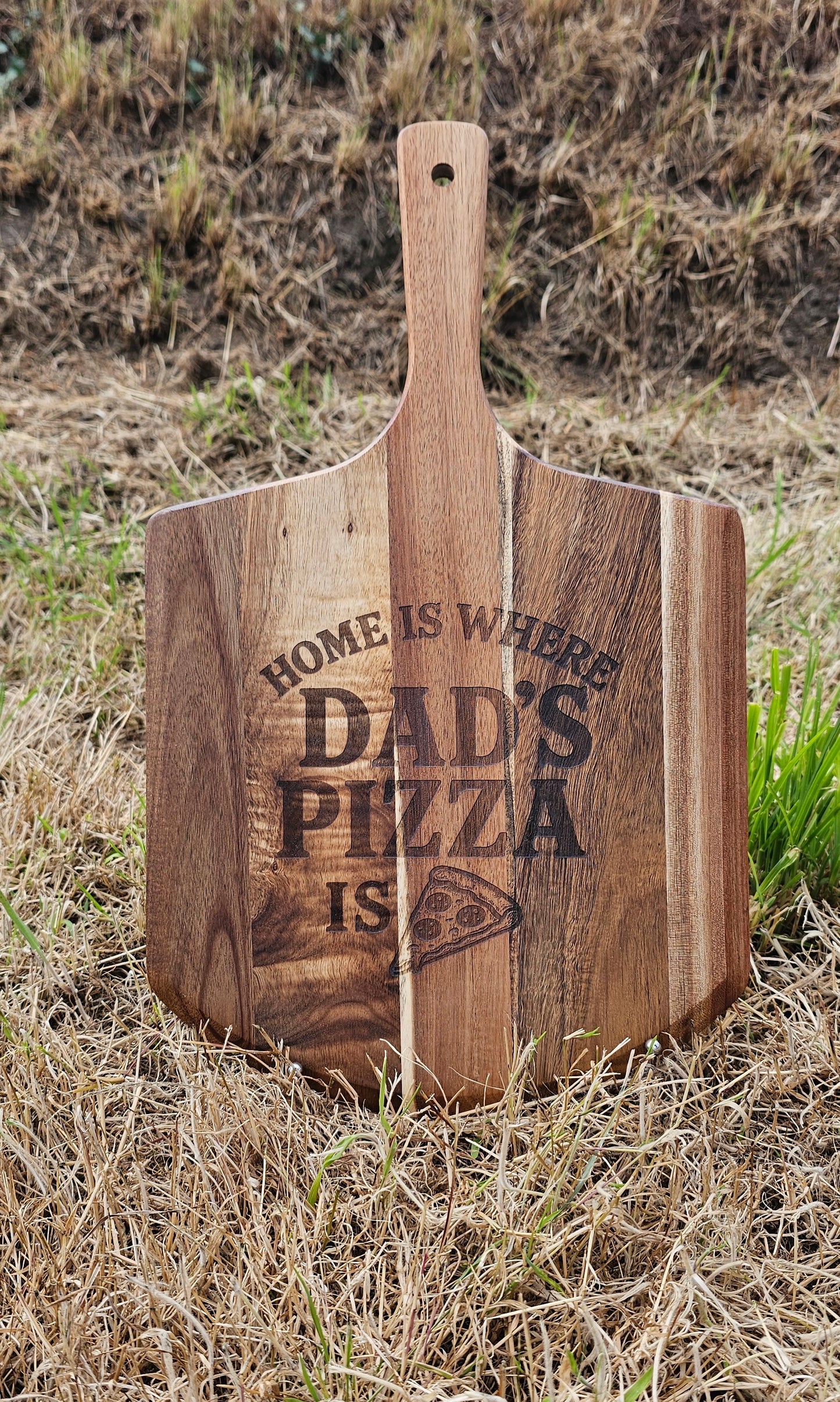 Wooden pizza peel with 'Home is where Dad's pizza is' engraving on grass