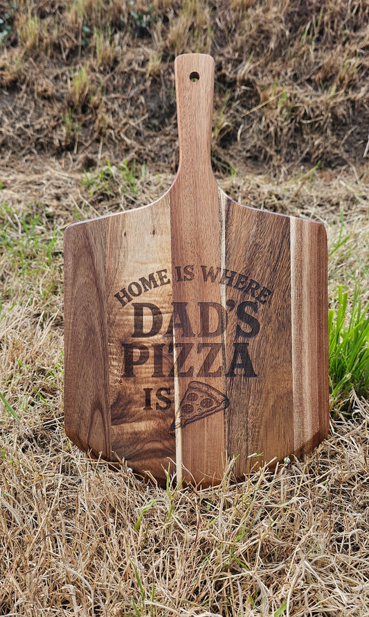 Wooden pizza peel with 'Home is where Dad's pizza is' engraving on grass