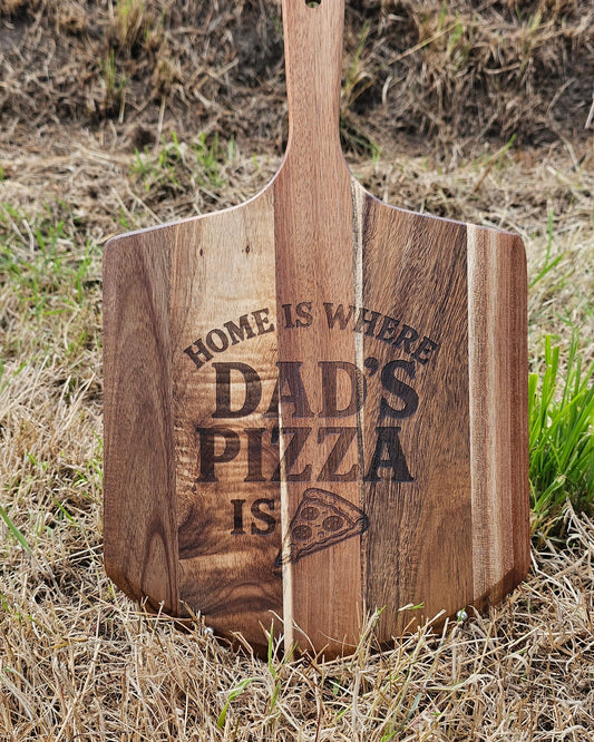 Wooden pizza peel with 'Home is where Dad's pizza is' engraving on grass