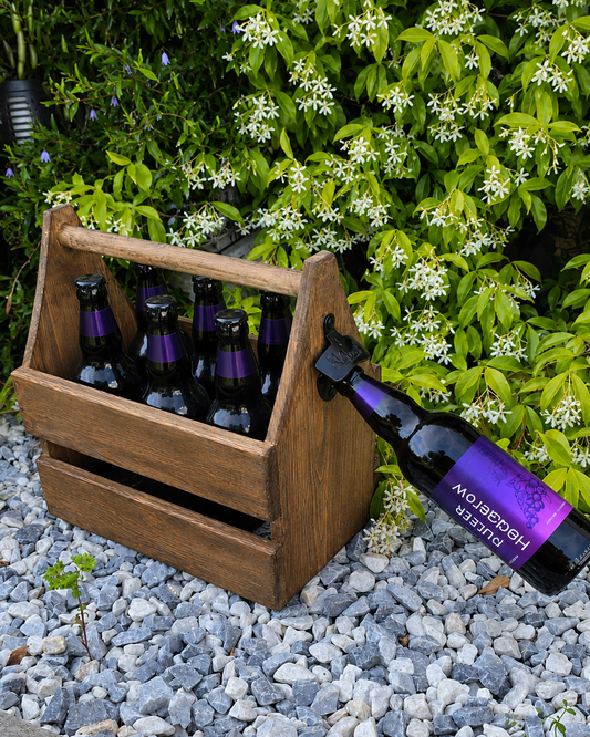 Wooden crate with beer bottles on a gravel surface with greenery in the background