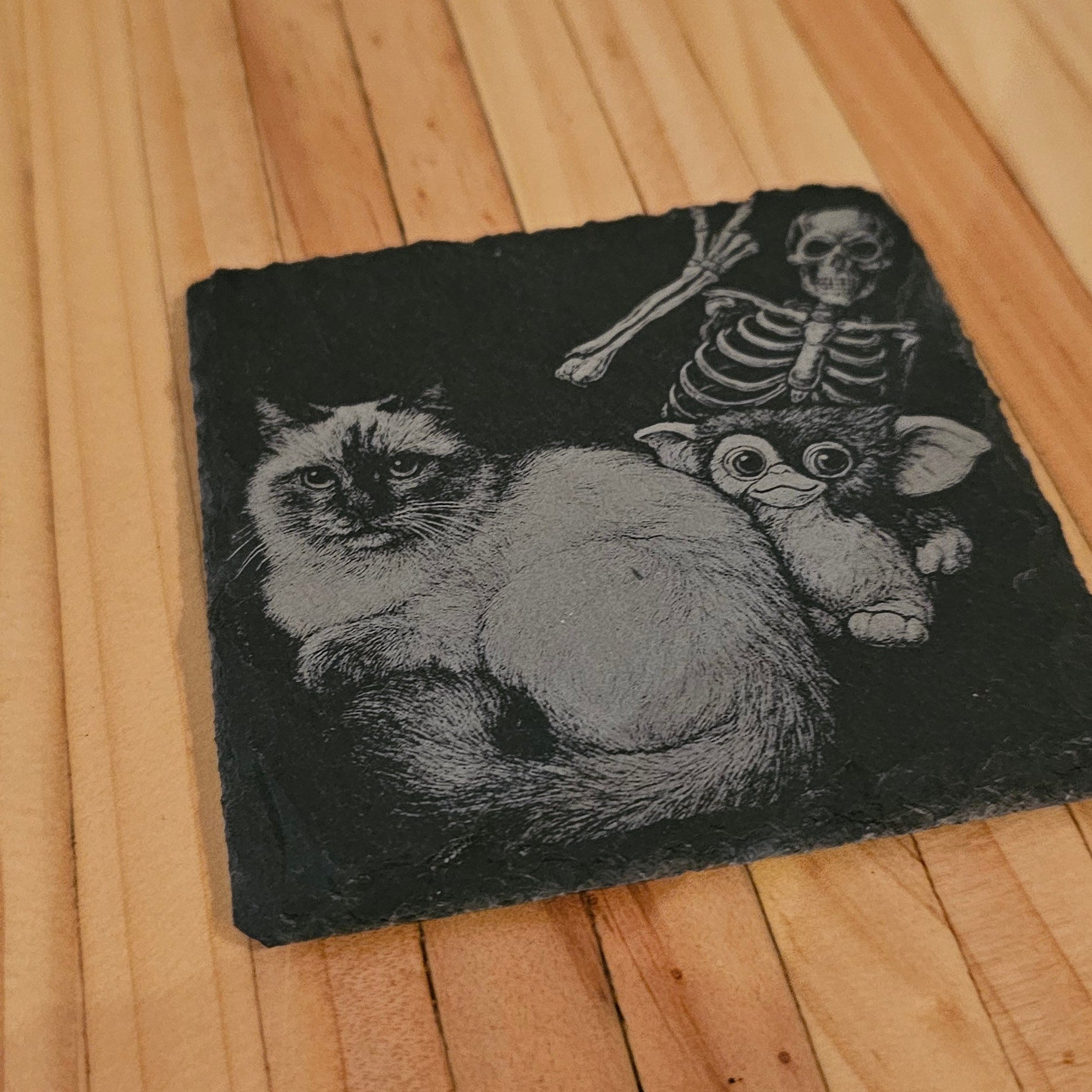 Black coaster with a skeleton and cat design on a wooden surface